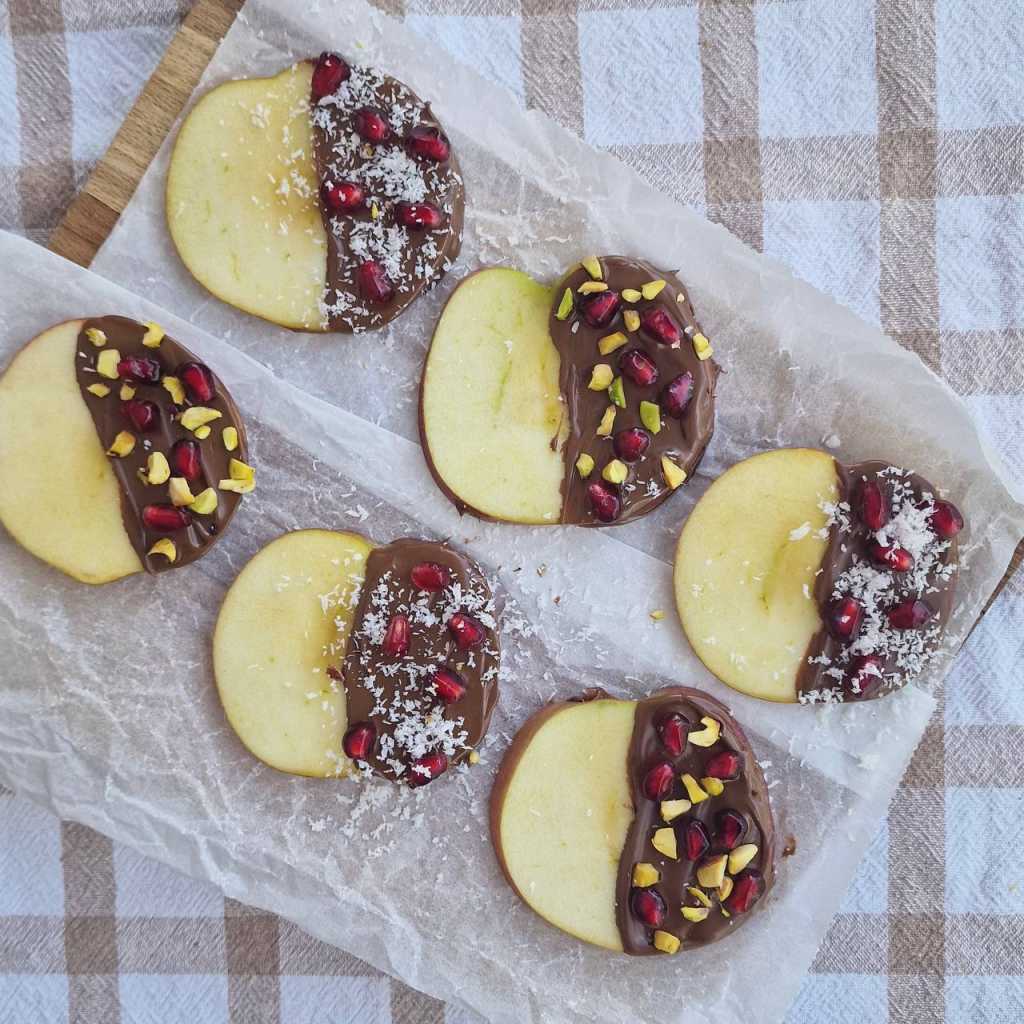 apple slices covered with chocolate pomegranate seeds, coconut flakes, pistachio nuts