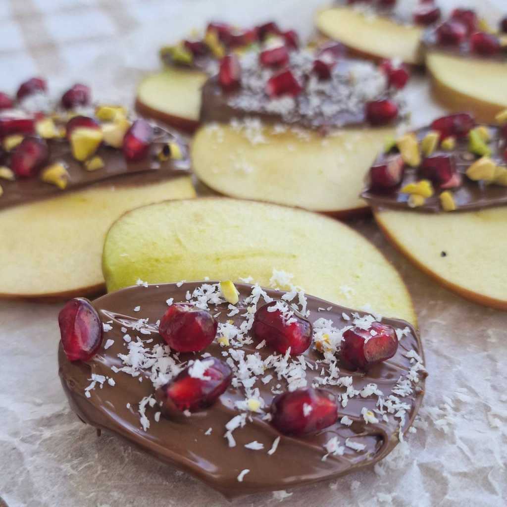 apple slices covered with chocolate pomegranate seeds, coconut flakes, pistachio nuts
