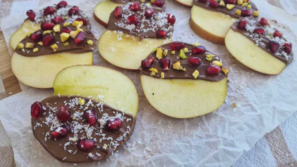 apple slices covered with chocolate pomegranate seeds, coconut flakes, pistachio nuts